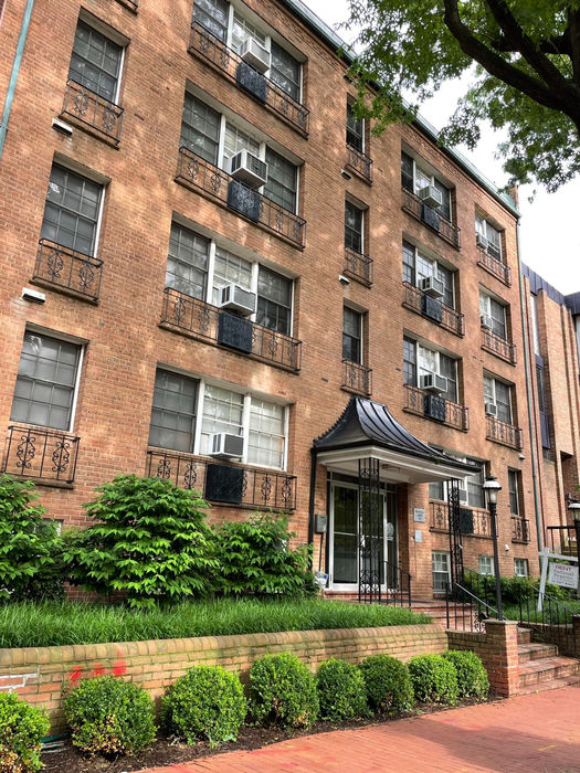 A sidewalk view of the front with a low brick retaining wall and curved metal canopy over front entry