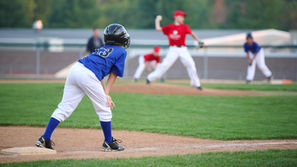 Photo of a youth baseball league, one player is on third base while the pitcher gets ready to release a pitch in the background.