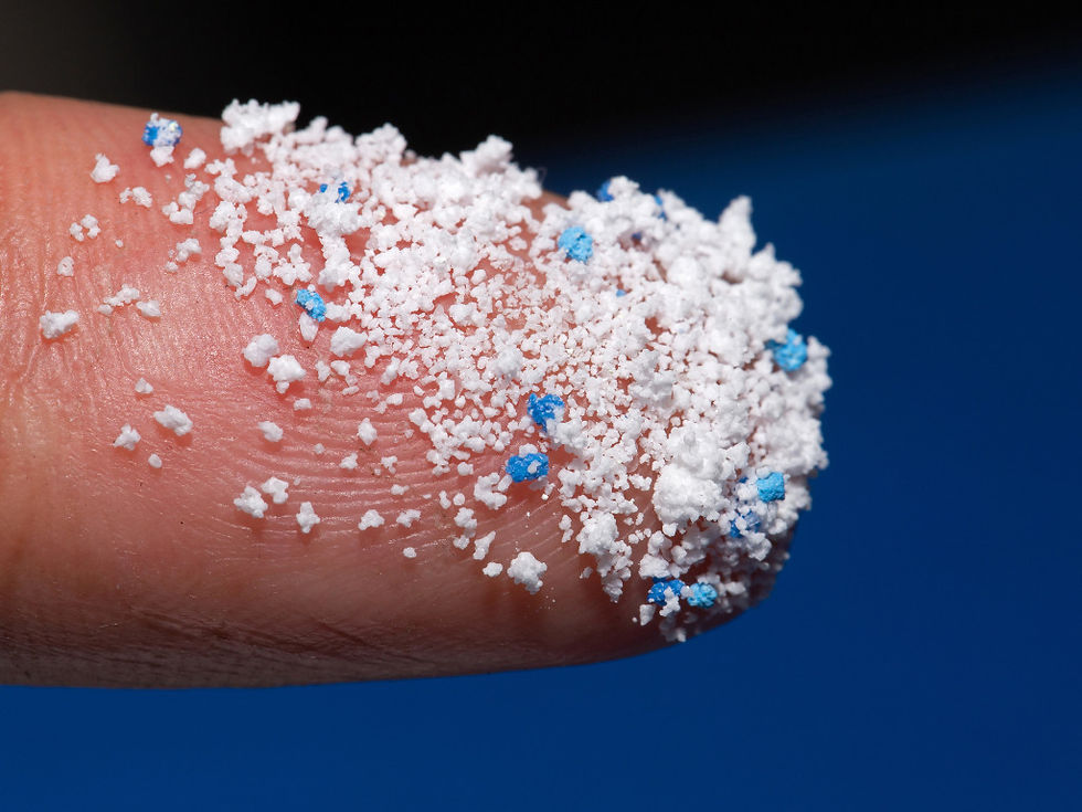 A close-up of a human finger covered in tiny white and blue microplastic particles against a blue background.