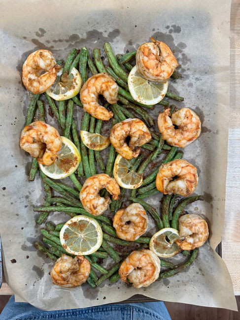 A sheet tray lined with parchment topped with baked shrimp, green beans, and lemon slices