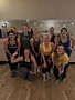 Group of women posing in a fitness studio, one flexing arm