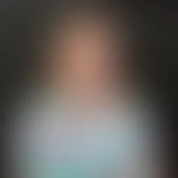 Photo over Melissa Griffin. Owner of Indigo Ink Interiors from valpo, but serving Indiana and Southern Michigan. She has red hair and is wearing a brightly colored mint shirt with red white and pink florals and is standing behind a black brick wall