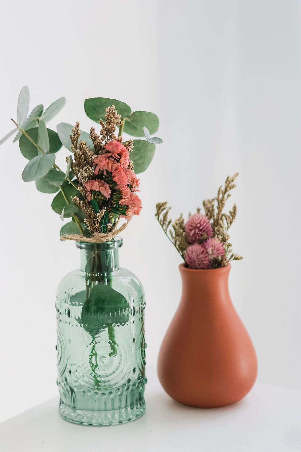 Decorative vases with dried flowers arranged on a neutral background_
