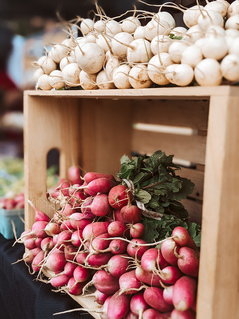 A wooden produce box with radishes on a black table cloth