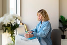 Woman seated at a desk writing in a notebook near a window_