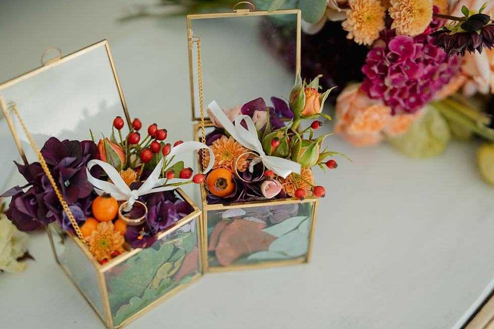 Two gold mirrored floral boxes with purple and orange flowers, berries, and white ribbons on a table.