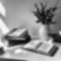 white desk flat lay with black books lit by sun grayscale.jpg
