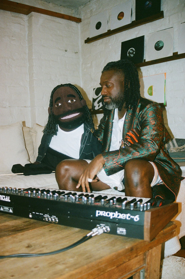 Singer and songwriter Aaron Taylor pictured with puppet, wearing Feng Chen Wang knitted set and embroidered luxury robe