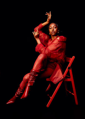 Singer and songwriter Anaiis sitting on red chair photographed on black backdrop, stylist Millie Cullum