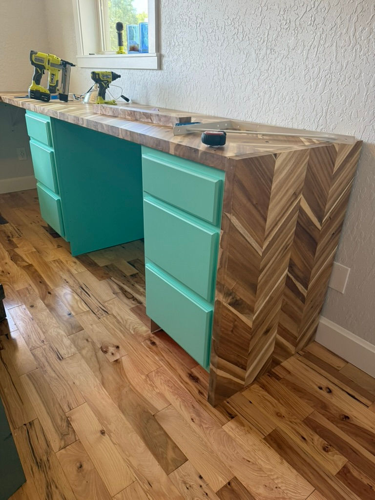 Two teal green cabinets with a butcher block desk sitting on top making a desk. In the process of being built with power tools sitting on top. 
