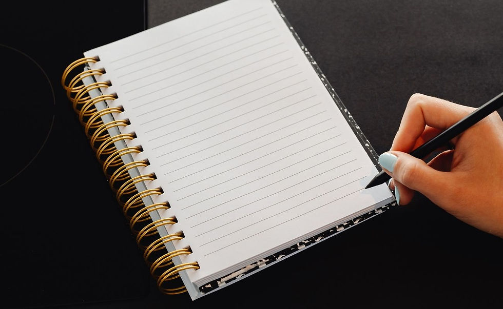 A person writing down in a notebook in front of a laptop.