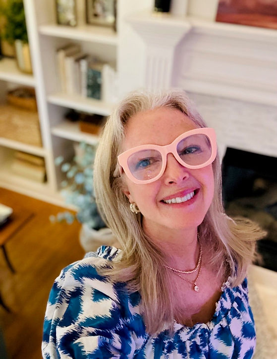 Ashley looks up, smiling, with pink glasses wearing a blue dress.