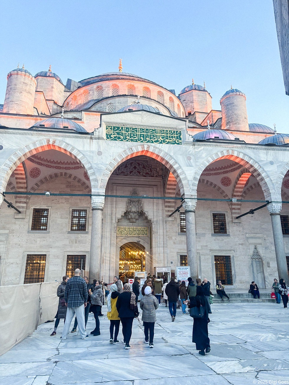 People gather outside the Blue Mosque with domes and arches at sunset. A sign reads "Closed." The sky is clear, and the mood is tranquil.