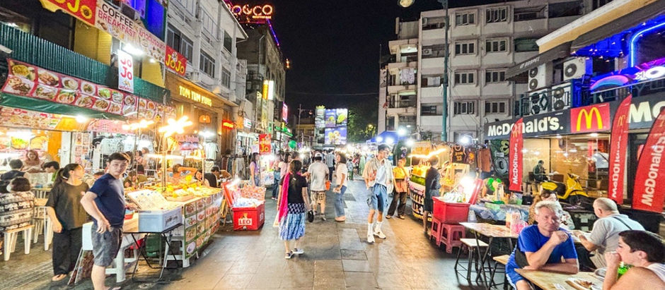 Bustling street market in Bangkok at night with food stalls, colorful signs, and people dining.