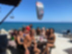 Group of people at a table, kite in sky, beach background, heavensurfhouse