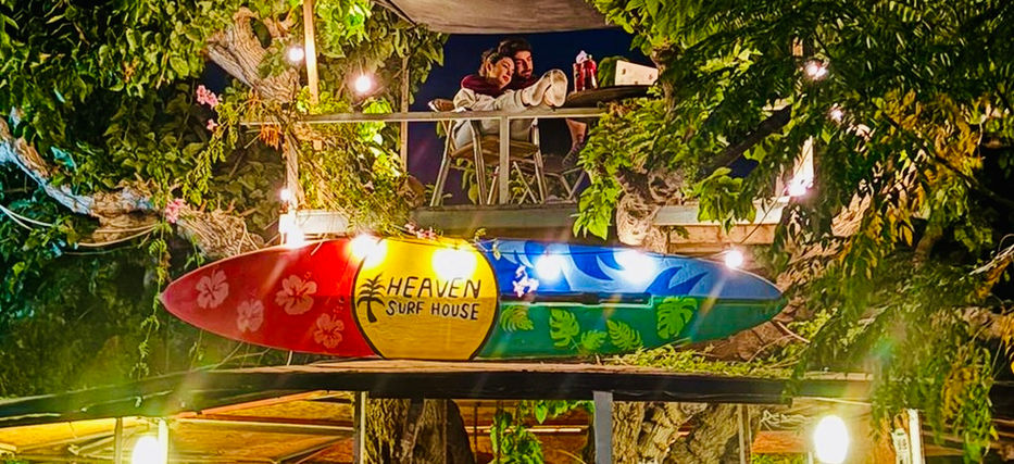 Colorful Aloha Bar sign with people inside and heavensurfhouse at night.