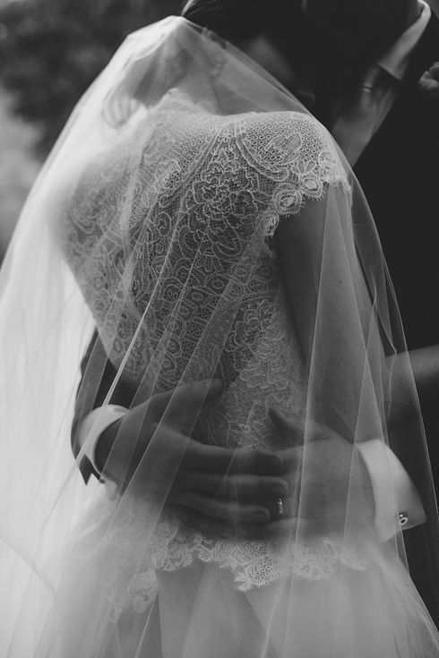 Black and white photo of a bride's back being hugged under the veil by her groom. Photo taken by Mariel Orellana, International luxury wedding photographer based in Antigua Guatemala.