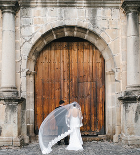 Bride about to walk down the aisle by the arm of her father in Capuchinas Convent in Antigua Guatemala. Stepping in front of the old wooden door of this convent in outside her luxury wedding venue. Photo by Mariel Orellana, international fine art and luxury wedding photographer and video.