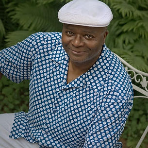 Smiling man in a white cap and blue polka dot shirt.