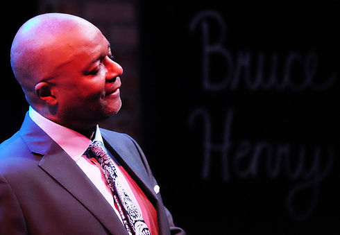 Bruce Henry in a suit, looking right, with his name in background.