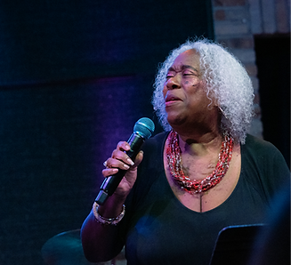 Woman with white hair singing into microphone.