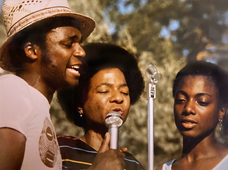 Man and woman singing into a microphone, another woman watching. 1970s archive.