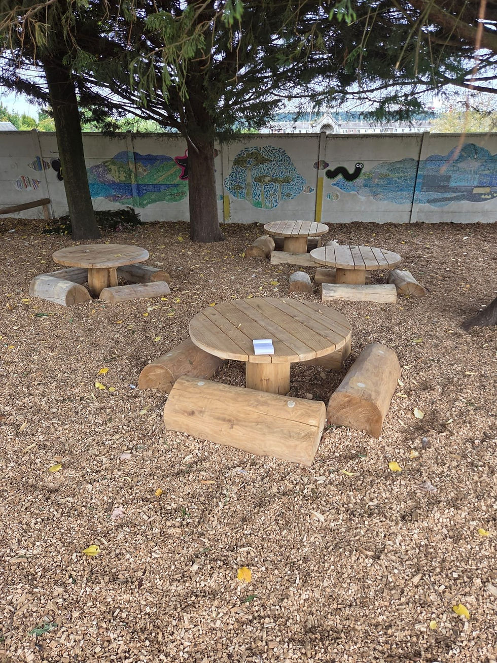 Tables rondes et bancs-rondins en acacia dans une cour d'école, sol en copeaux de bois