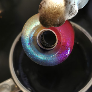 A pair of tongs gripping a wheel with two colours applied to it. A pan of dye bath is in the background