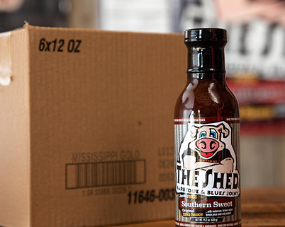 A bottle of The Shed and Blues Joint BBQ sauce in front of a case of bottles ready to be shipped