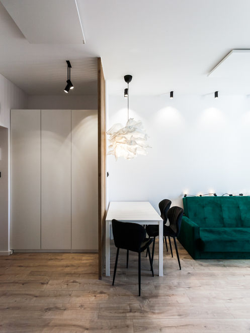 Elegancki salon z zieloną sofą, jadalnią, jasnymi szafami, drewnianą podłogą.