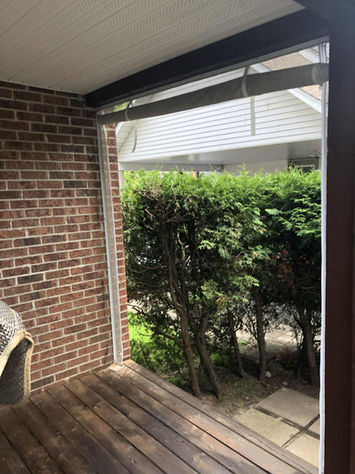 Porche avec mur de briques, verdure et rideau transparent. Auvents Signature.