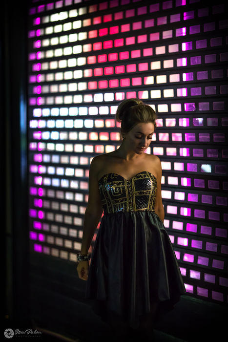 A person stands in front of a colorful illuminated wall, showcasing intricate patterns on the back of their garment.