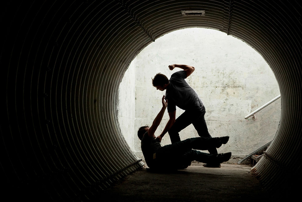 Two people in a tunnel, one standing, about to punch the other on the ground. Dimly lit, tense atmosphere, concrete background.