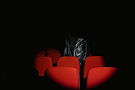 A black leather motorcycle jacket is in silhouette in between red movie theatre seats.