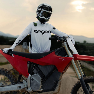 A motorcyclist with helmet on, standing behind his motocross bike