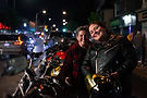 Two women motorcyclists similing in front of their bikes, helmets in hand.