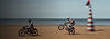 Two bikes riding on the beach. One is doing a wheely.