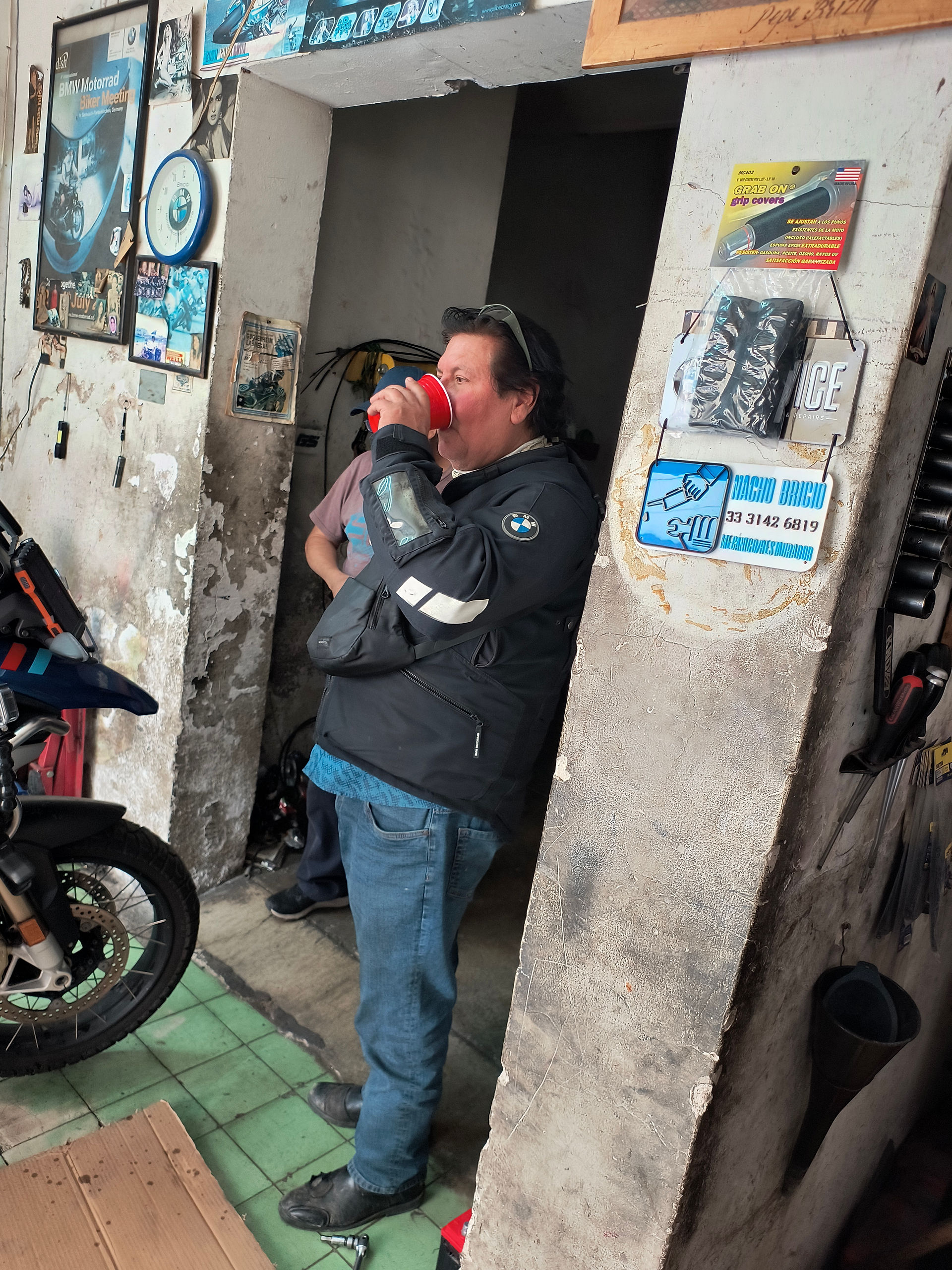 A man drinking a coffee outside of an old motorcycle repair shop
