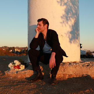A man sitting on the ground next to a pillar with a bouquet of flowers beside him.