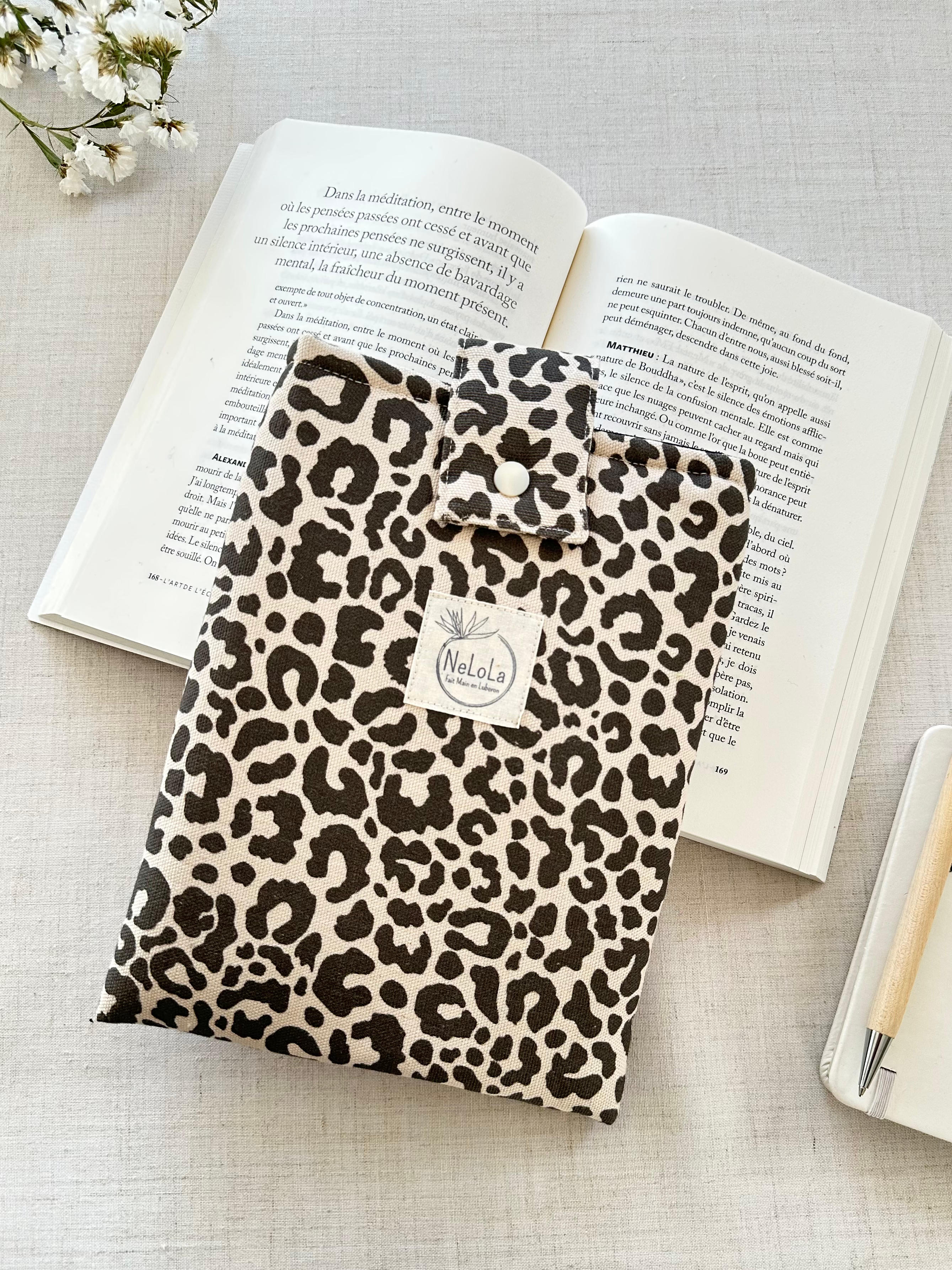 Pochette à livre rembourrée Tanzanieen tissu léopard beige et marron cousue main, posée devant un livre ouvert