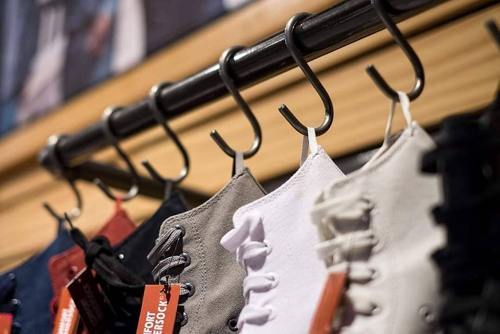Several pairs of sneakers in grey, white, and black, displayed hanging from black hooks on a metal rail inside a Levi’s store