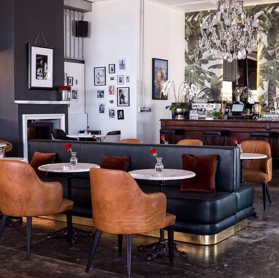 Cozy lounge seating area with leather chairs, dark booth seating, marble-topped tables, small vases with red flowers, and a c