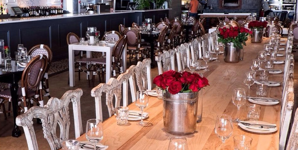 Long wooden dining table set with glassware, plates, and silverware, surrounded by ornate white chairs and decorated with met