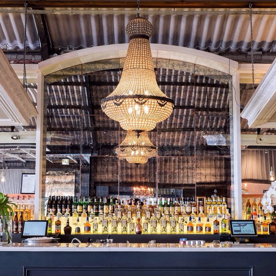Elegant bar area with a large beaded chandelier hanging in front of a mirrored backdrop, bottles of liquor neatly arranged be
