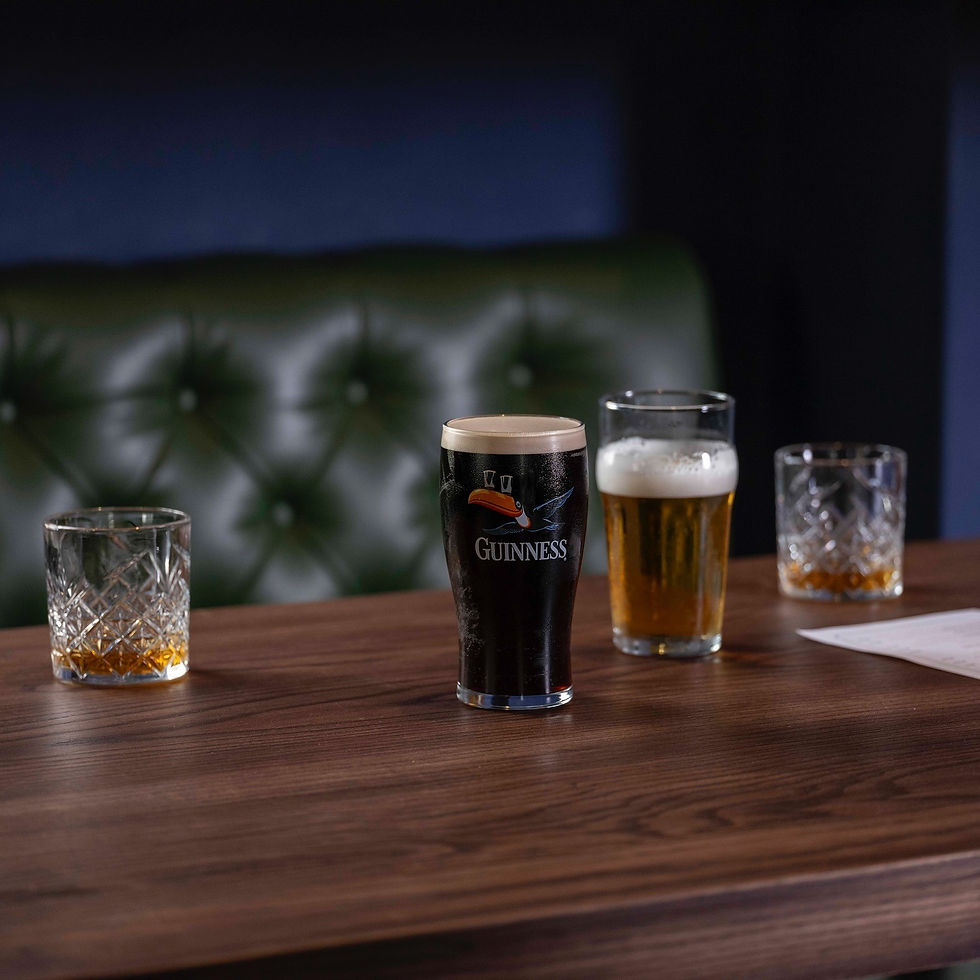 A pint of Guinness, a glass of beer, and two whiskey glasses on a dark wooden table with green leather booth seating in the b