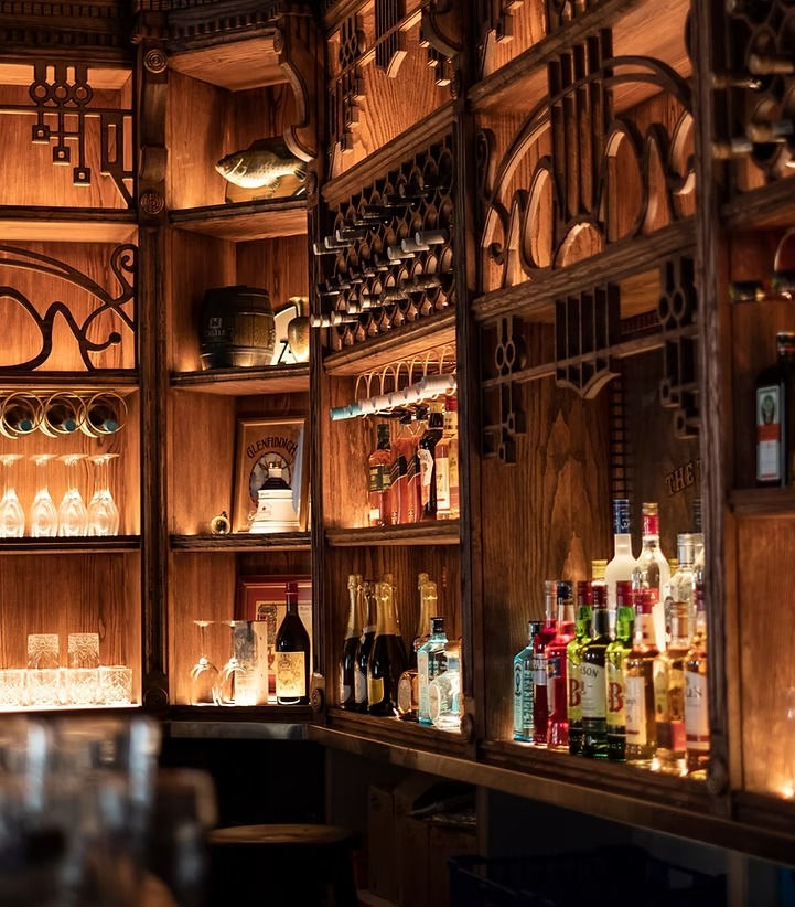 The Twelve Bells bar interior with illuminated wooden shelves, liquor bottles, wine racks, and carved woodwork, viewed from a
