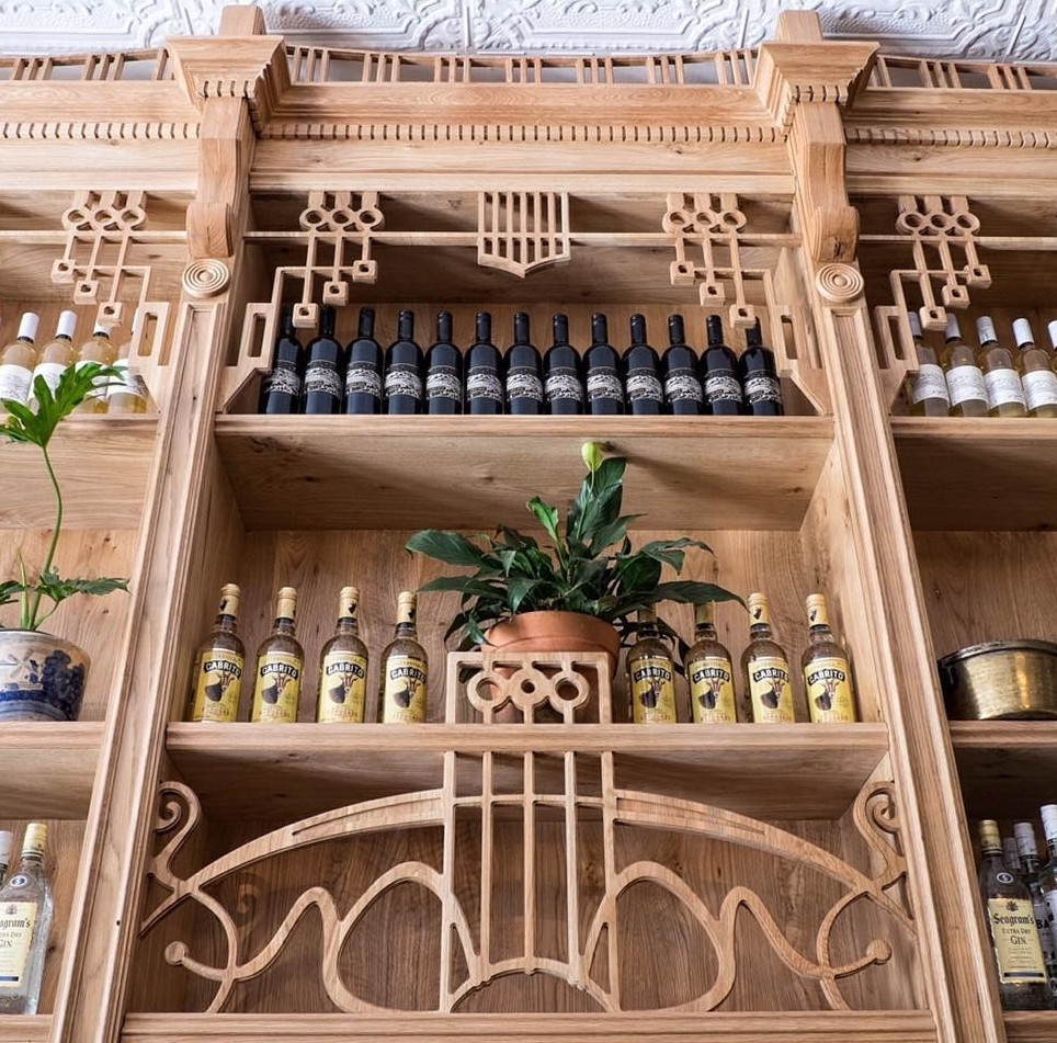 Close-up of The Sorrows bar shelving showcasing wine bottles, tonic bottles, a potted plant, and detailed wooden latticework