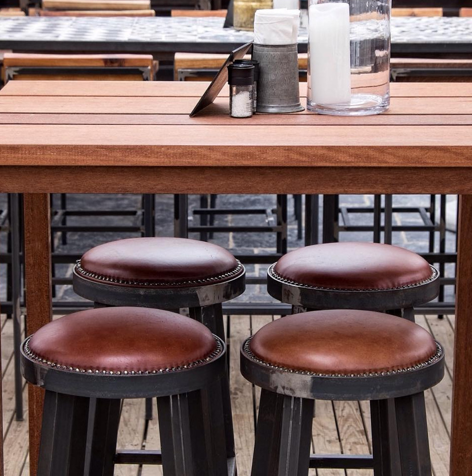 Close-up of a wooden table with leather bar stools – Four brown leather round bar stools tucked under a high wooden table wit
