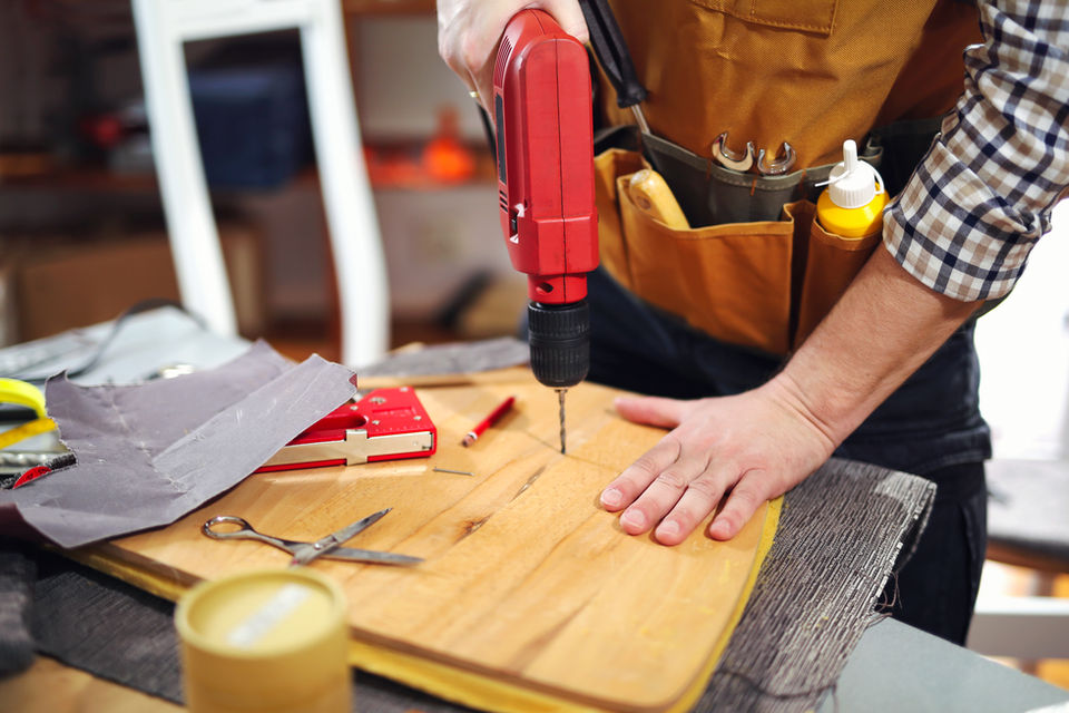 Man using red electric drill to bore into wooden board.