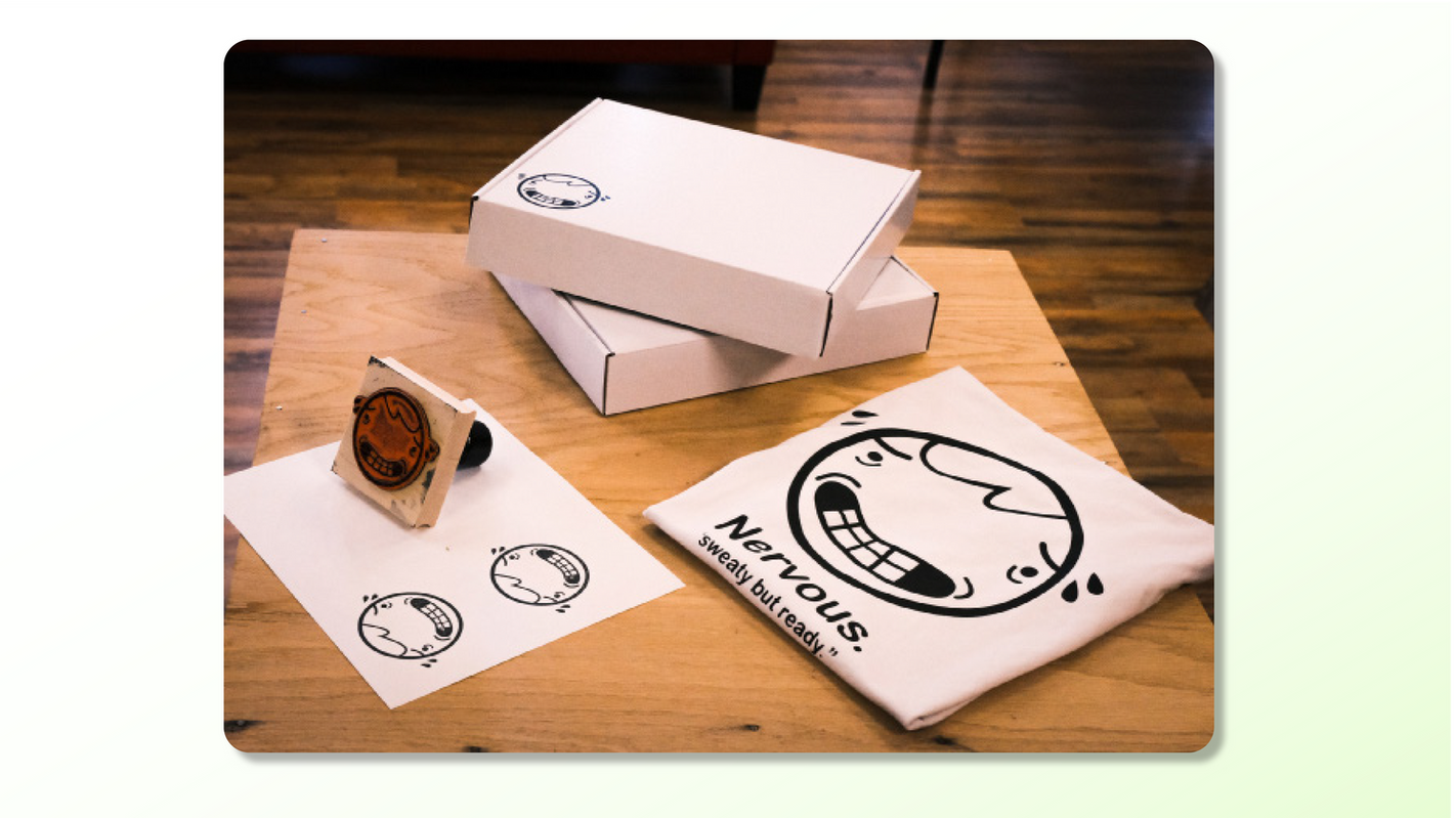 Nervous Box promotional product photo featuring custom anxiety-inspired smiley logo, stamped subscription box, and folded graphic tees for a mental health apparel brand.